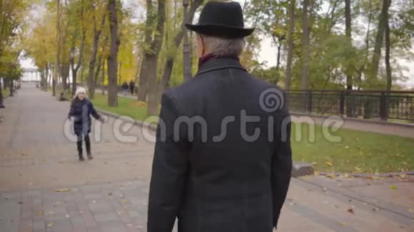 一位戴着优雅黑色帽子和外套的高加索人的后景等待他的孙女跑起来把她养大视频的预览图