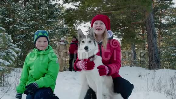 快乐的女孩少年拥抱狗在雪地森林的冬天散步友好的家庭在冬天一起散步狗冬季视频的预览图