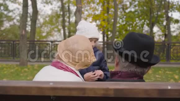 一对高加索人夫妇坐在长凳上听着一个欢快的微笑女孩在前面跳跃视频的预览图