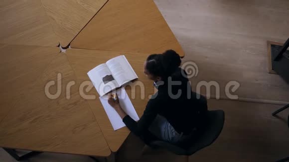 吸引人的集中非洲年轻女子坐在书桌旁在她的大学笔记簿上做一些笔记视频的预览图