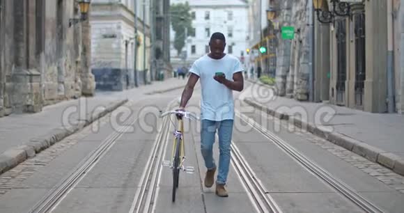 穿着休闲装的英俊肌肉发达的非裔美国人年轻人用他的智能手机和时髦的现代自行车视频的预览图