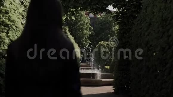 长头发的女孩去喷泉沿着小巷在迷宫的绿色灌木丛在一个花园后景女人休息视频的预览图