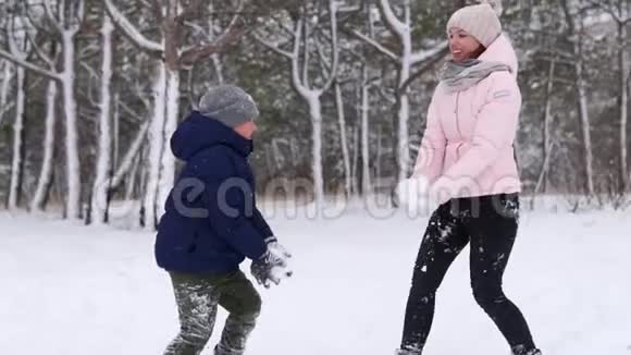 快乐的母亲和儿子在寒冷的冬天玩雪把它扔到森林里的空气中女人和男孩视频的预览图