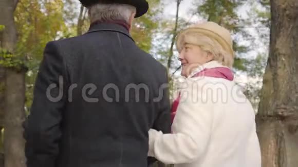一位穿着米色紧身衣的白种人成熟女性在秋天公园的丈夫旁边散步视频的预览图