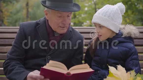 一位穿着经典服装的白种人成年男子与孙女坐在长凳上读着一本书视频的预览图