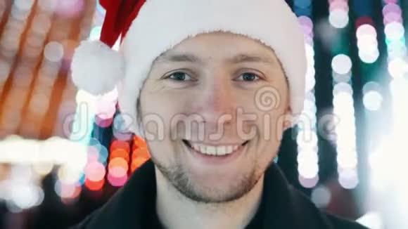 年轻开朗的男子肖像戴着新年帽子微笑看着相机圣诞花环的灯光视频的预览图