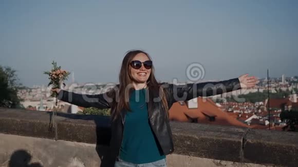 戴墨镜和皮夹克的微笑女孩站在有手臂的房子屋顶的石墙附近视频的预览图