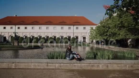 漂亮的年轻女士背包坐在池塘的栏杆上瓦伦斯坦宫和池塘里有鱼和视频的预览图