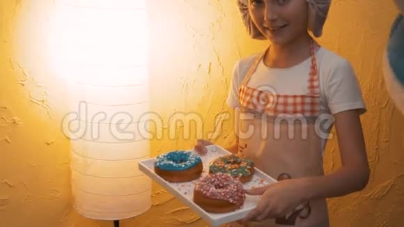 年轻的厨师女孩拿着托盘和五颜六色的釉面圈快乐的女厨师在厨房的帽子准备了烹饪甜甜圈视频的预览图
