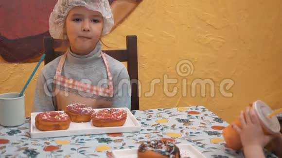 可爱的女孩戴着厨师帽吃甜甜圈从杯子里喝可可小女孩用吸管吃甜甜圈视频的预览图
