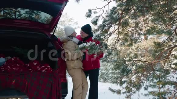 幸福的一对相爱的情侣在雪地森林里笑着在红色的汽车背景下在冬天散步微笑的男人和女人玩得开心视频的预览图