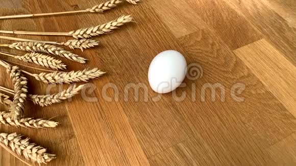 据一位妇女报道一个白色的鸡蛋躺在一张木桌上上面放着成熟的麦穗和鸟毛视频的预览图