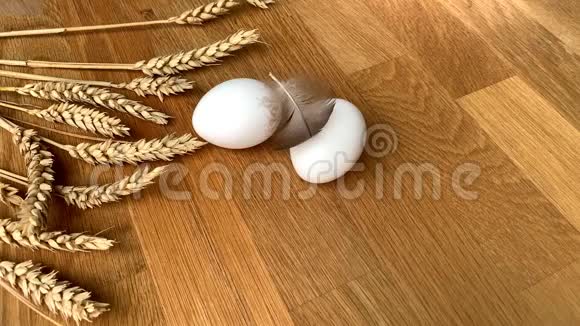 据一位妇女报道两个白色的鸡蛋放在一张木桌上上面放着成熟的麦穗和鸟毛视频的预览图