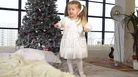 穿着白色连衣裙身后有圣诞树的小女孩跳得真有趣视频的预览图