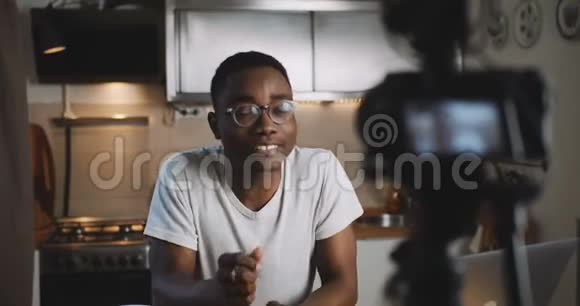 快乐年轻成功的黑人vlogger男子拍摄视频为他的在线博客与相机在家厨房慢动作视频的预览图