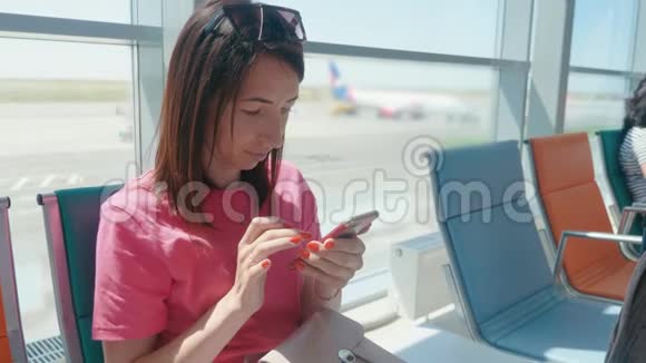 一个年轻漂亮的女孩坐在机场候车室用手机女人买电子机票做酒店视频的预览图