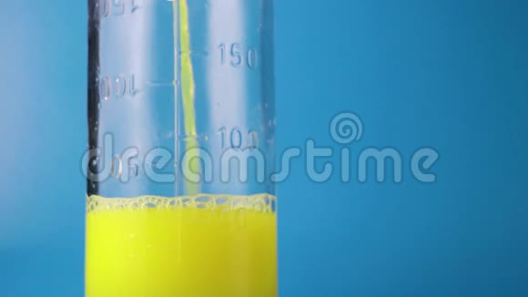 黄色液体倒入玻璃中在蓝色背景上测量瓶视频的预览图