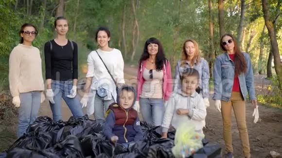 妇女和孩子们在林地的垃圾堆旁用手指摆出胜利的手势快乐而欢快视频的预览图