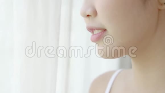 一个年轻的亚洲女人醒来喝着一杯水窗户是新鲜的视频的预览图