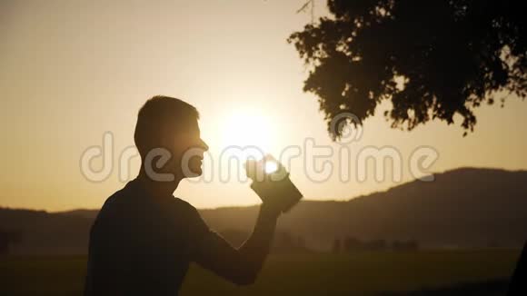一个身材匀称的年轻人在日落时喝着带有太阳的水的轮廓视频的预览图