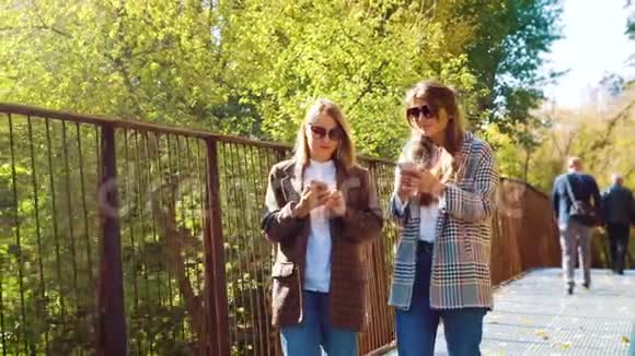 带着智能手机在阳光公园的桥上行走的旅行博主视频的预览图