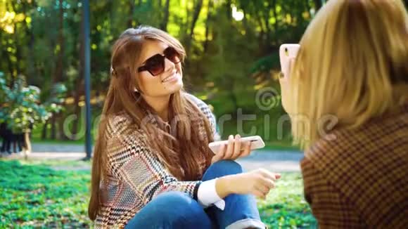 快乐的女孩浏览社交媒体和朋友聊天秋天公园视频的预览图