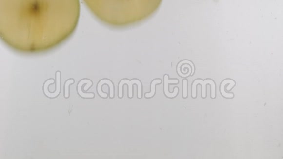 慢动作新鲜的绿色苹果切片掉在水里白色的背景上有飞溅和气泡视频的预览图