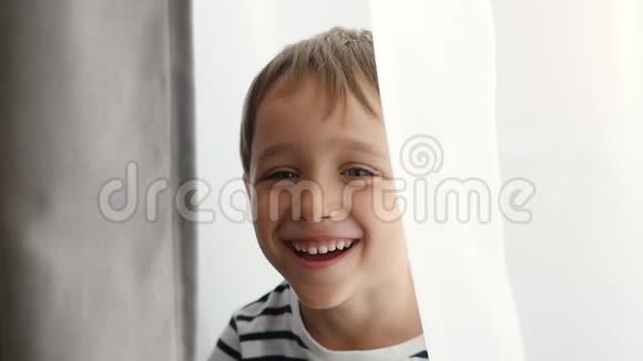 孩子在窗口玩捉迷藏一个可爱的小男孩看着相机展示了情感幸福视频的预览图