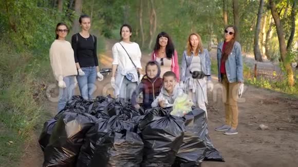 一队志愿者生态学家在清理森林领土后在一堆垃圾袋附近摆姿势一起微笑视频的预览图
