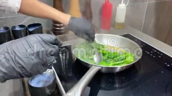 厨师在金属锅上菜搅动菠菜叶子视频的预览图