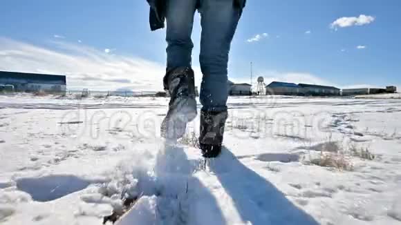 在一个冬天阳光明媚的日子里跟随着穿着牛仔裤和温暖鞋子在雪地里行走的男人特写低角度回去视频的预览图