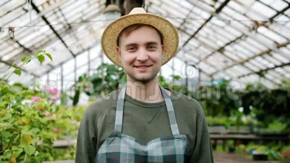 戴着帽子和围裙的英俊男子农民站在温室里的肖像视频的预览图