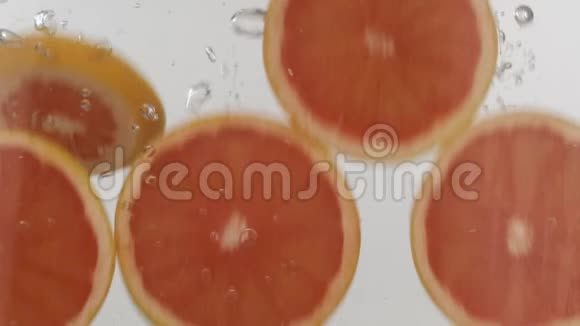 慢动作新鲜切片葡萄柚掉进水中白色背景上有飞溅和气泡视频的预览图