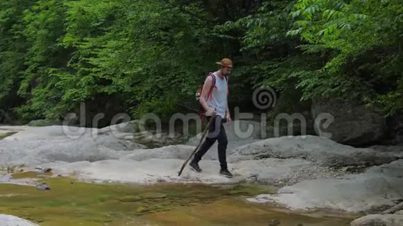 一个孤独的年轻人沿着一条干净的山河沿着峡谷的底部行走视频的预览图
