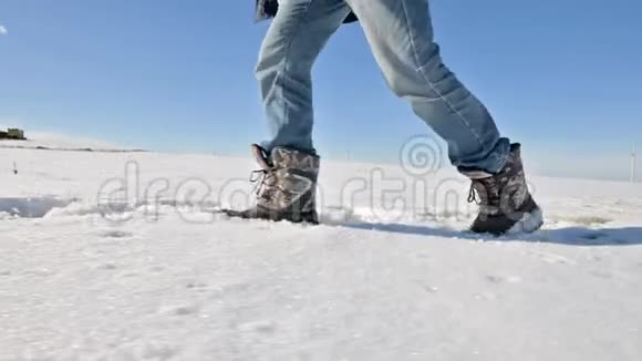 在一个冬天阳光明媚的日子里跟随着穿着牛仔裤和温暖鞋子在雪地里行走的男人特写低角度侧面视频的预览图