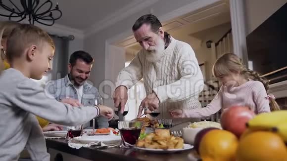 感恩节庆祝期间一家人在餐桌上闲荡祖父在餐桌上切烤火鸡视频的预览图