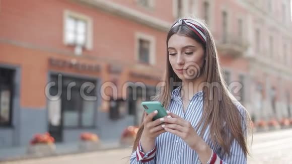 年轻漂亮时尚的女孩棕色头发戴着头巾穿着条纹连衣裙用她的智能手机语音指挥视频的预览图