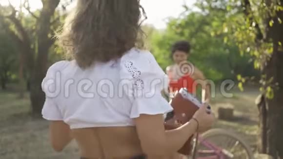 可爱的白种人年轻女性留着短发在她的朋友在花园或公园拍照时用自行车摆姿势视频的预览图