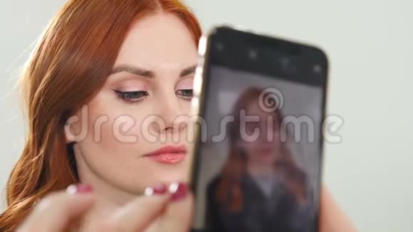 一位年轻的红发美女在美容院用电话拍摄的特写镜头微笑快乐的女孩视频的预览图