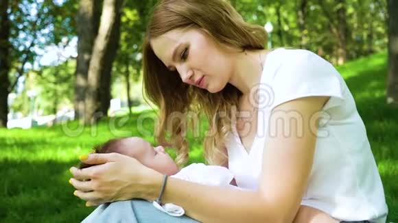 可爱的小宝宝睡在坐在公园里的年轻妈妈的膝上视频的预览图