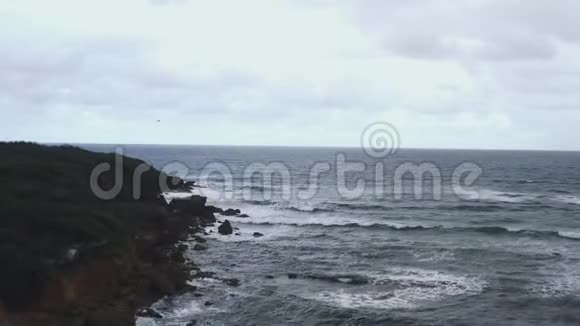 当海浪溅上岸时沿着岩石海岸线飞行的空中射击视频的预览图