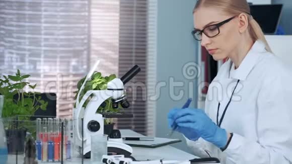 女化学教授用镊子把有机材料放在幻灯片上然后在显微镜下观察视频的预览图