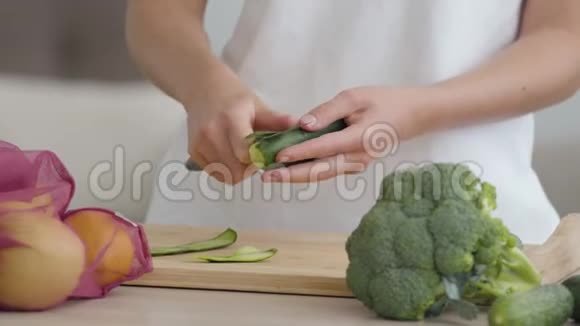 年轻苗条的女人用锋利的刀在厨房的桌子上削黄瓜概念视频的预览图