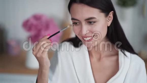 美丽女人的肖像化妆用画笔在她的眼睛上画眼影视频的预览图