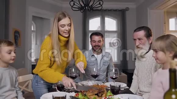 一位长得很漂亮的女士为她的亲戚雕刻美味的烤火鸡她坐在节日的家庭餐桌旁视频的预览图