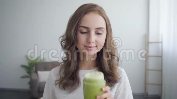 一幅年轻微笑的女人在家厨房的摇床里闻着冰沙的肖像健康食品的概念视频的预览图