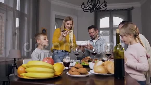 微笑的金发母亲在家庭宴会上把意大利面放在盘子里视频的预览图