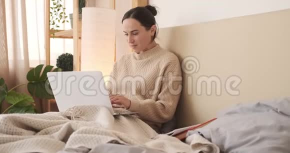 在床上使用笔记本电脑和写笔记的女人视频的预览图