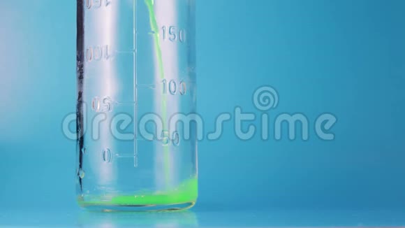 绿色液体倒入蓝色背景的玻璃量瓶中视频的预览图