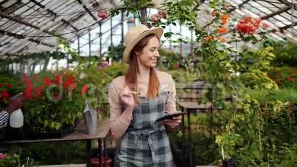 在温室计数植物中使用平板电脑的快乐女人的慢动作视频的预览图
